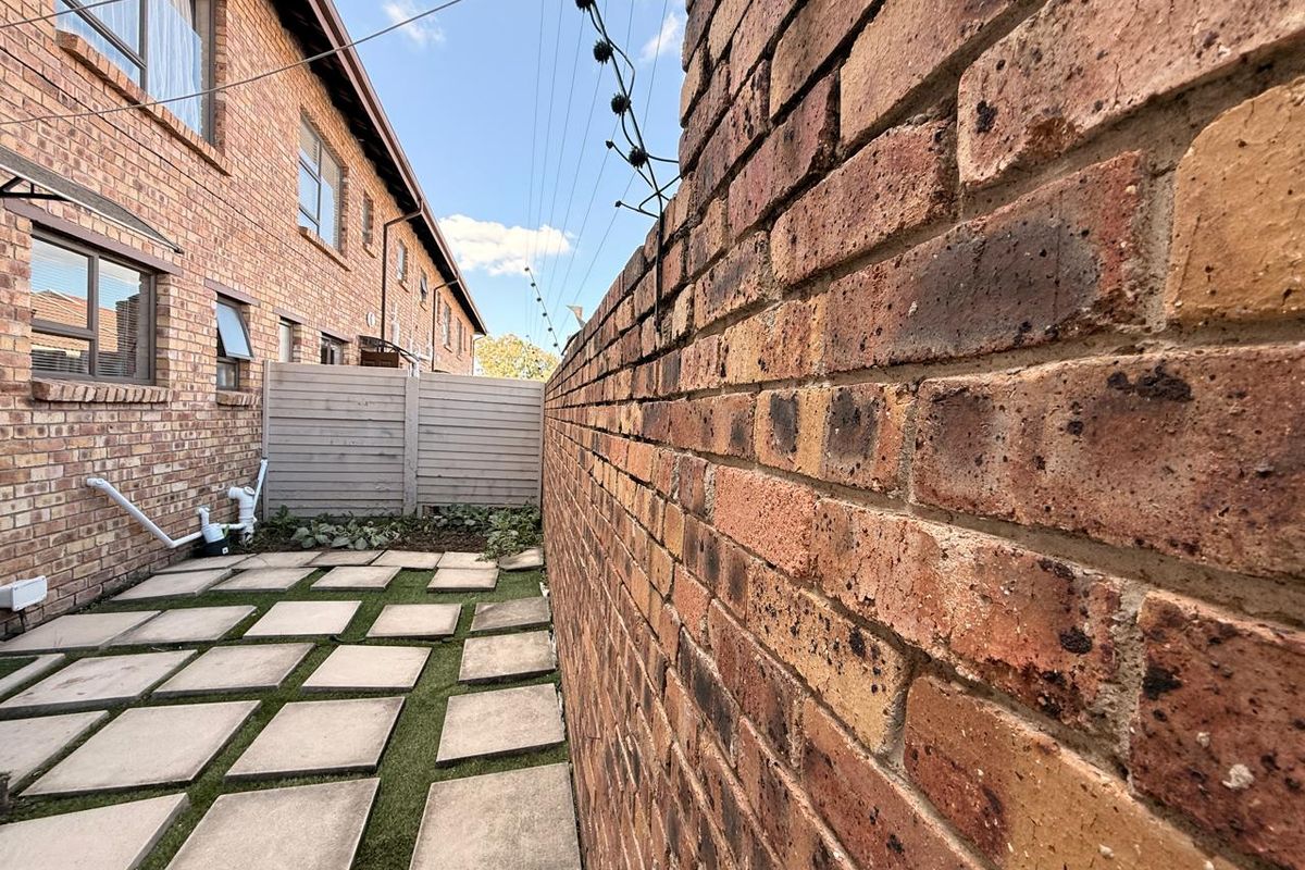 A rear courtyard area featuring a face brick boundary wall with electric fencing, paved stepping stones, and artificial grass maintenance-free landscaping.
