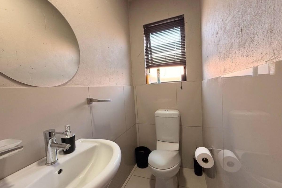 A compact bathroom featuring a pedestal basin, toilet, and tiled finishes, requiring minor cosmetic attention to the wall surfaces.