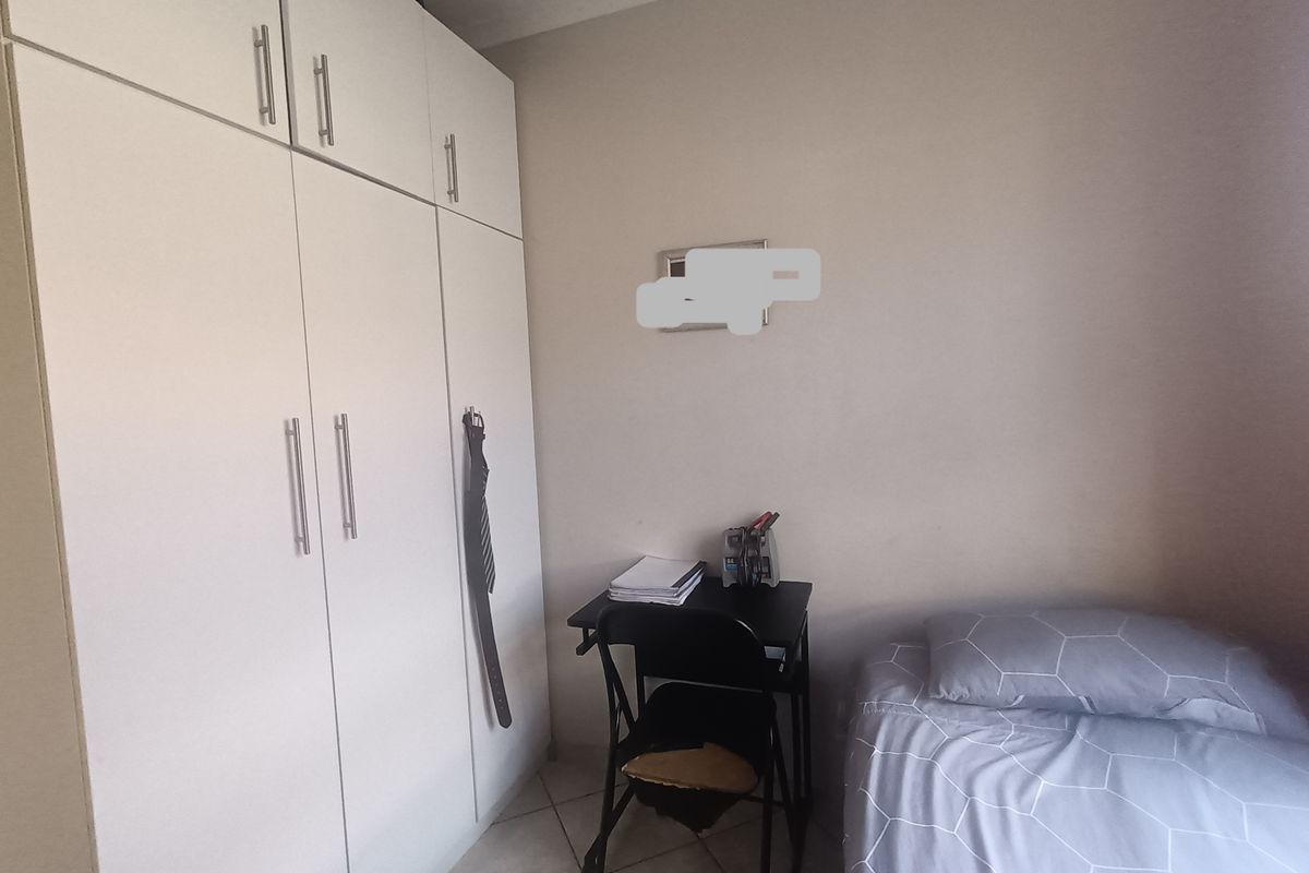A compact bedroom featuring built-in floor-to-ceiling white cabinetry and tiled flooring.