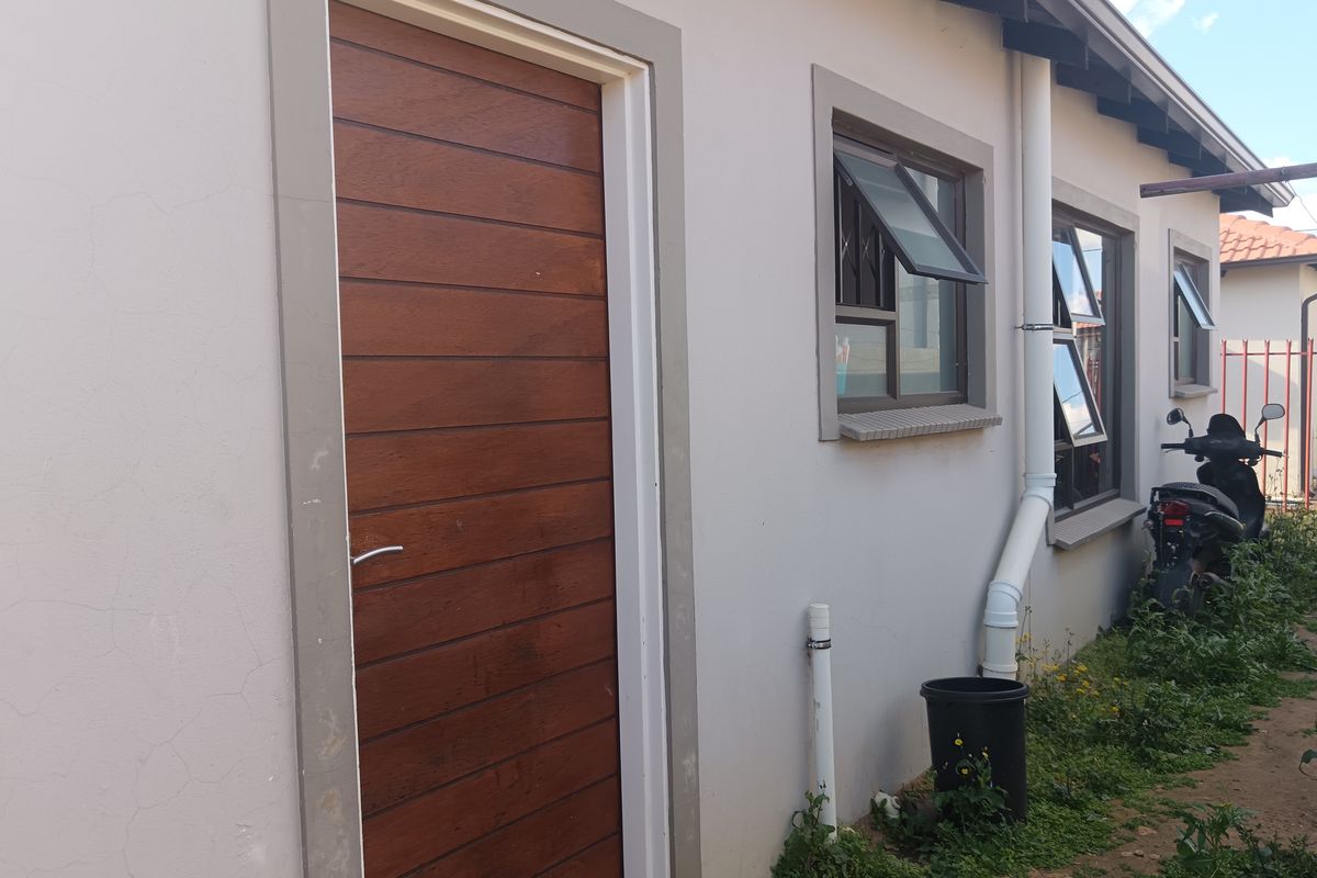 A view of the side exterior elevation featuring a modern timber-look door, aluminium window frames, and exposed downpipe infrastructure.