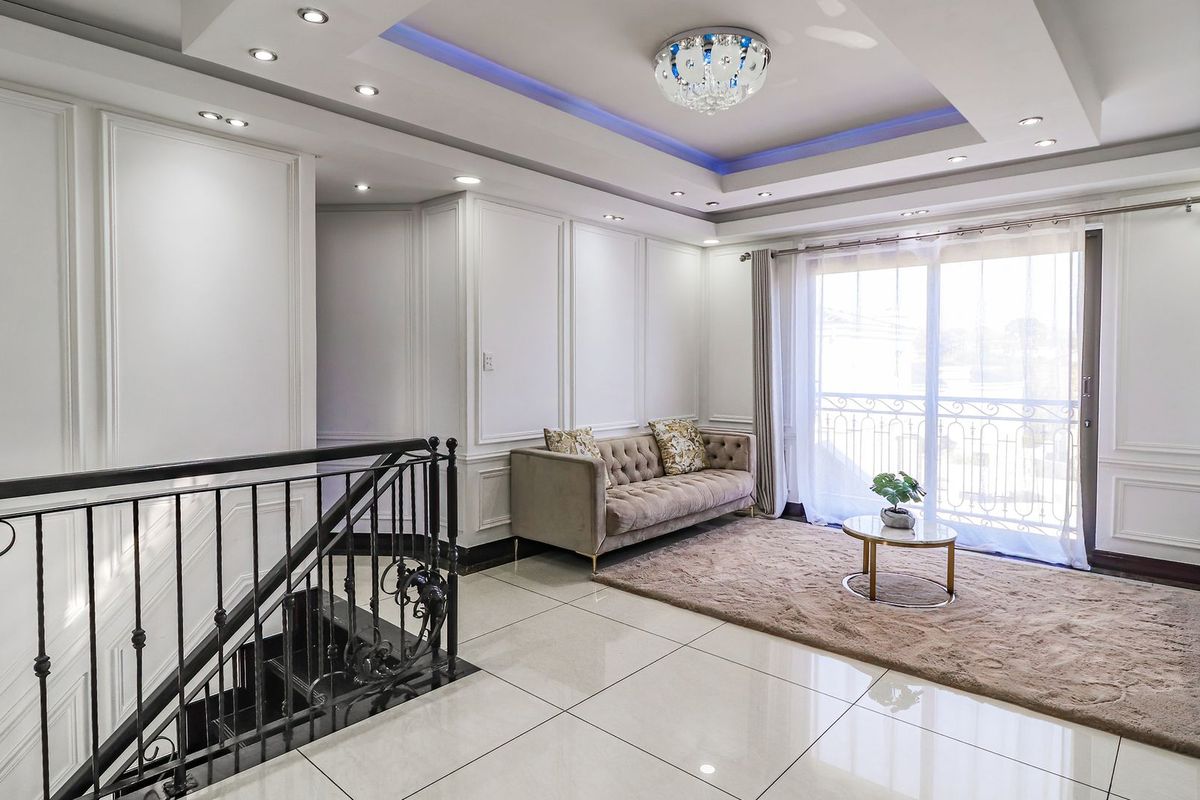 Elegant living room featuring sophisticated wainscoting, recessed ceiling lighting with cove accents, polished tile flooring, and direct access to a balcony via sliding glass doors.