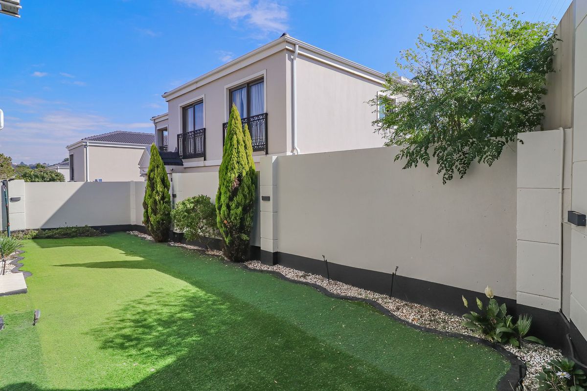 A well-maintained rear garden featuring a neat artificial lawn, high boundary walls for privacy, and modern exterior wall lighting.