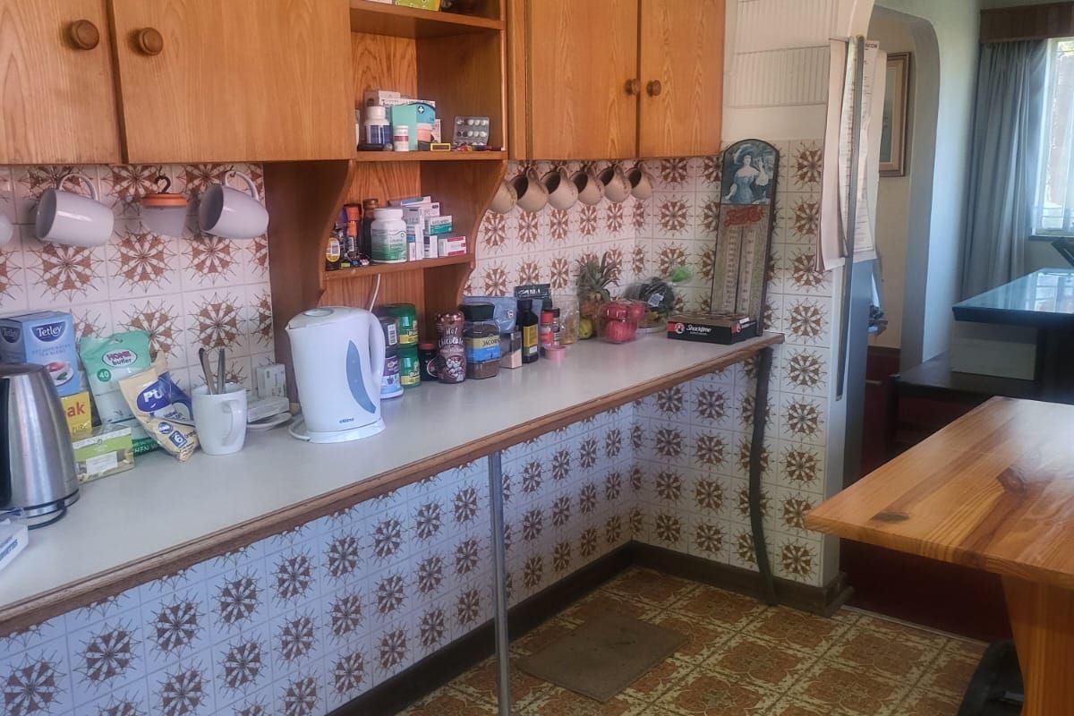 A dated kitchen area featuring original patterned wall and floor tiles, wooden cabinetry, and an arched entryway leading to the adjacent living space.