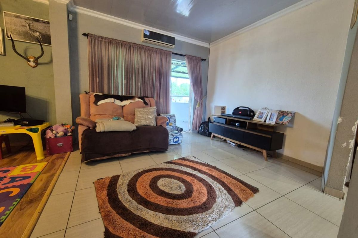 A living room featuring tiled flooring, a wall-mounted air conditioning unit, and sliding door access to an outdoor area.