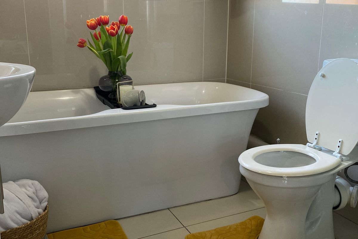 A modern bathroom featuring a freestanding bathtub, a wall-mounted toilet, and neutral floor-to-ceiling wall tiles.