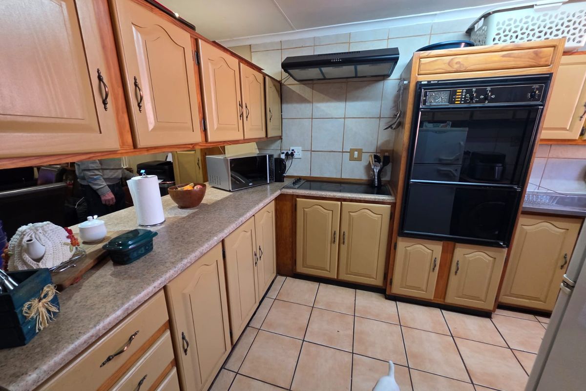 A functional kitchen featuring traditional timber cabinetry, a built-in eye-level oven, a ceramic hob, and a tiled backsplash with neutral floor tiles.