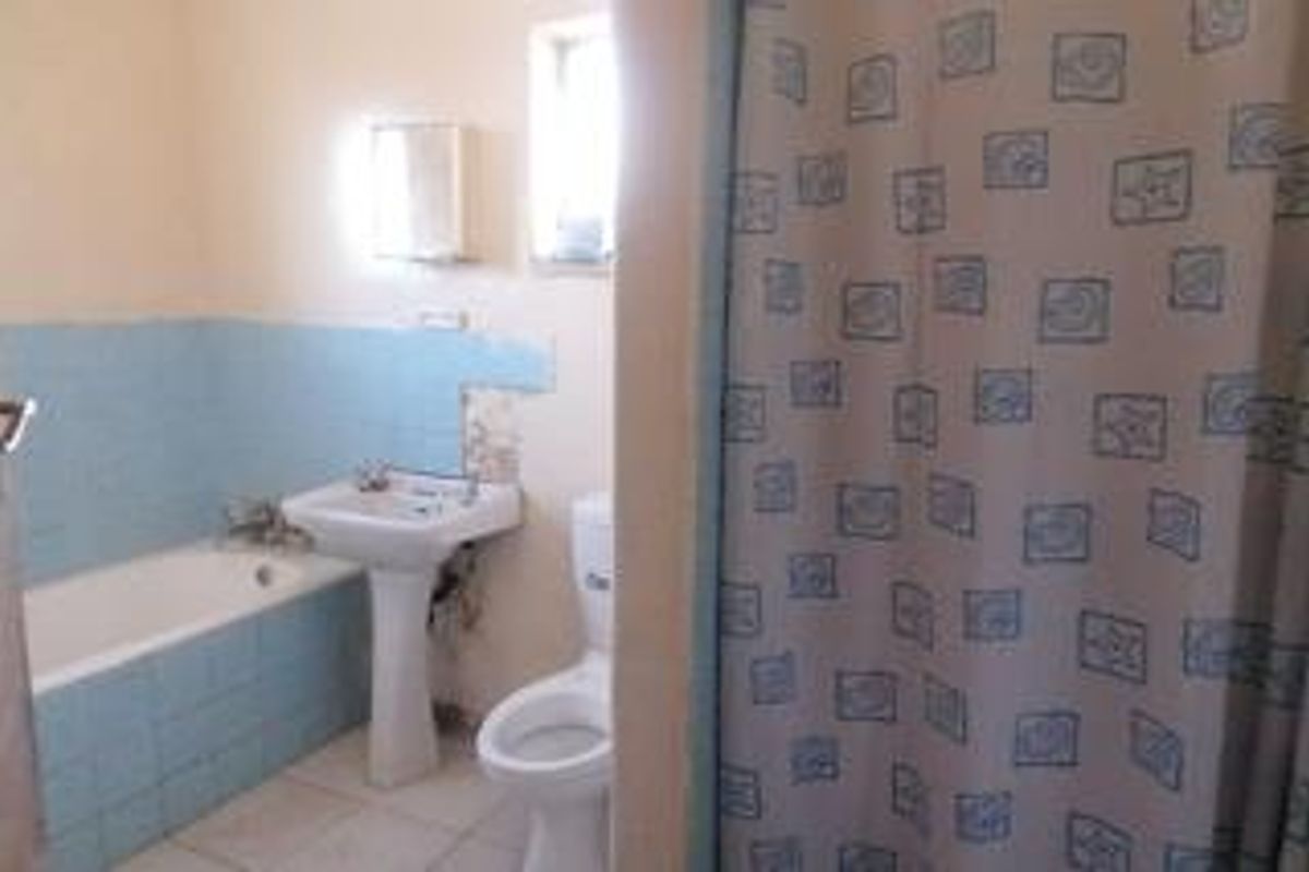 A functional bathroom featuring a bathtub with blue tiled surround, pedestal basin, and toilet, requiring some cosmetic updates to the wall finishes.