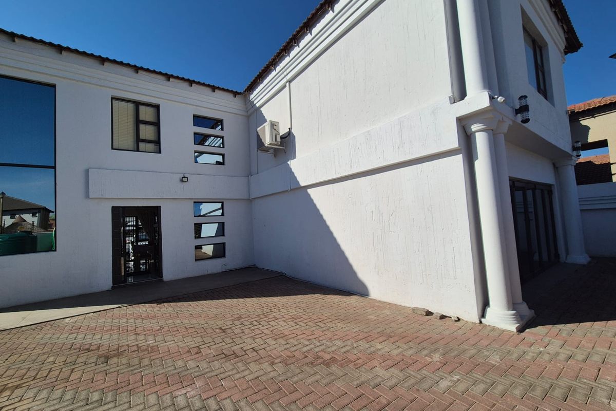 A view of the rear exterior of the house featuring white rendered walls, paved courtyard, and architectural columns.