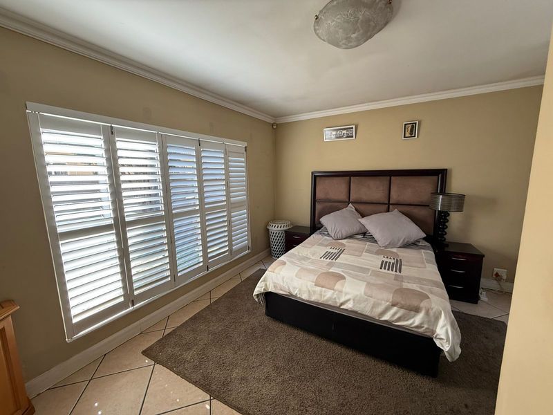 A bedroom featuring tiled flooring, crown molding, and white plantation shutters on the window.