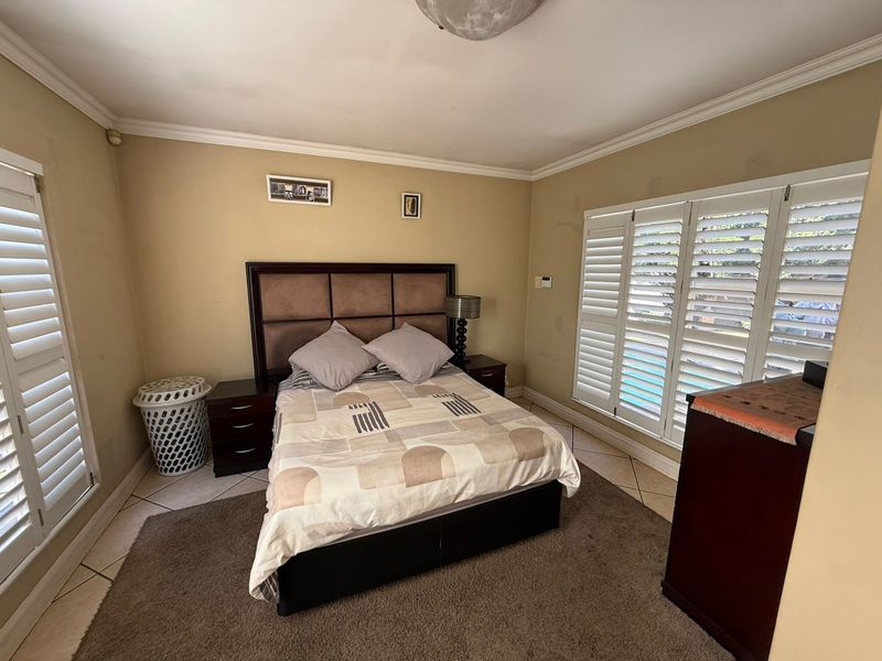 A well-lit bedroom featuring tiled flooring, crown molding, and white plantation shutters on the windows, providing a comfortable and functional living space.