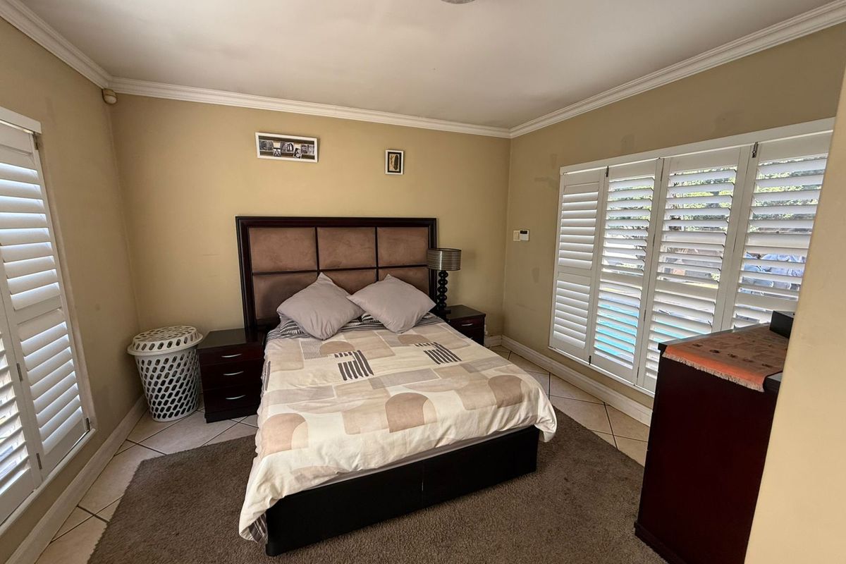 A well-lit bedroom featuring tiled flooring, crown molding, and white plantation shutters on the windows, providing a comfortable and functional living space.