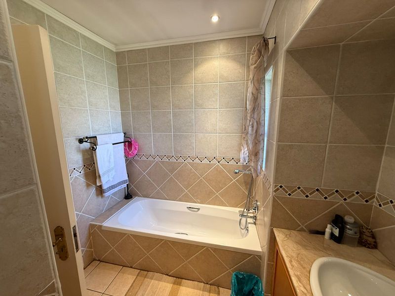 A functional bathroom featuring a built-in bathtub with tiled surround, integrated vanity basin, and neutral wall tiling.