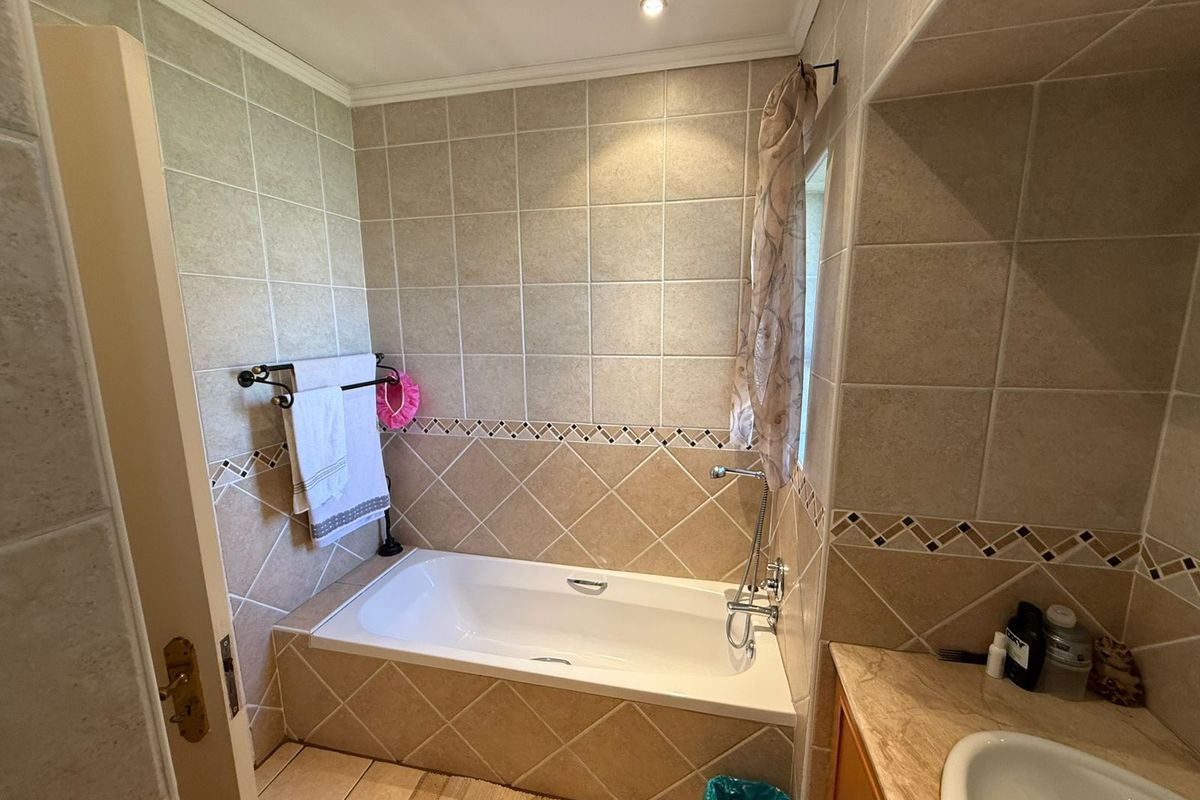 A functional bathroom featuring a built-in bathtub with tiled surround, integrated vanity basin, and neutral wall tiling.