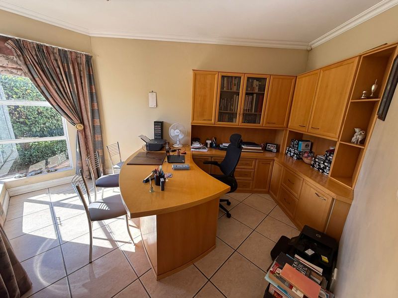 A functional home office featuring built-in wooden cabinetry, tiled flooring, and large windows providing natural light.