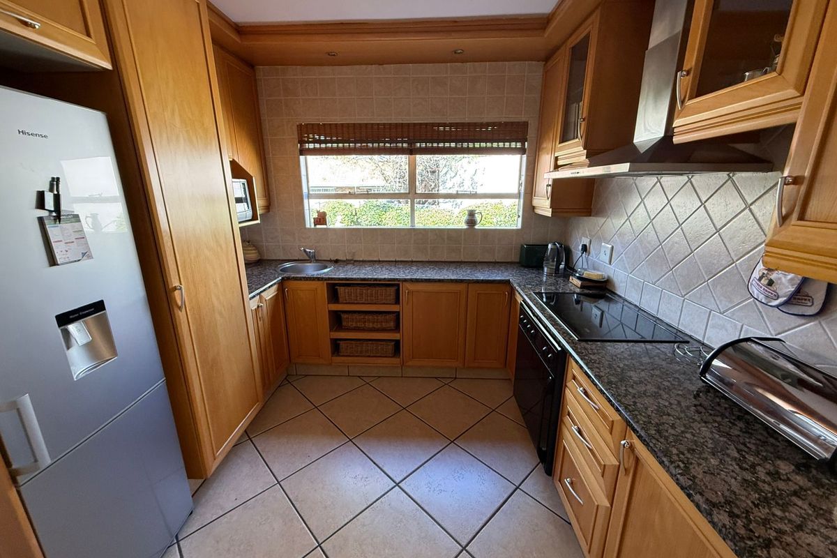A functional kitchen featuring wooden cabinetry, granite countertops, a built-in hob, extractor fan, and tiled flooring with a window overlooking the garden.
