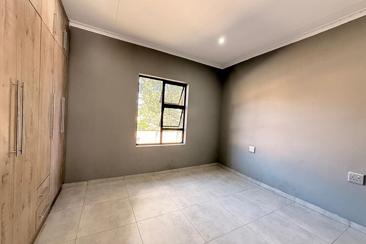 A bright, empty bedroom featuring modern tiled flooring, neutral grey walls, and extensive built-in wooden cabinetry.