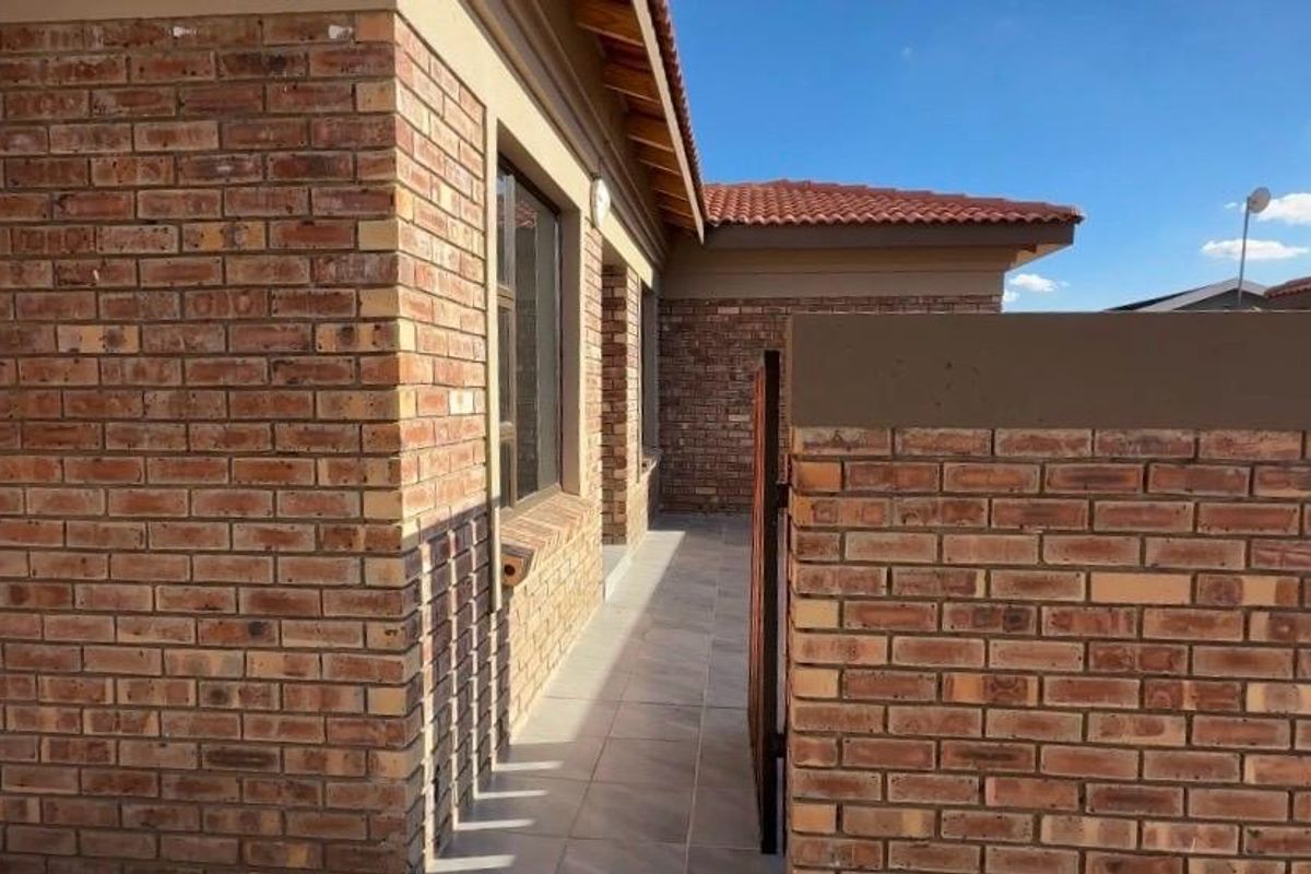 A side walkway of the townhouse featuring face-brick exterior walls, tiled flooring, and a secure boundary wall.