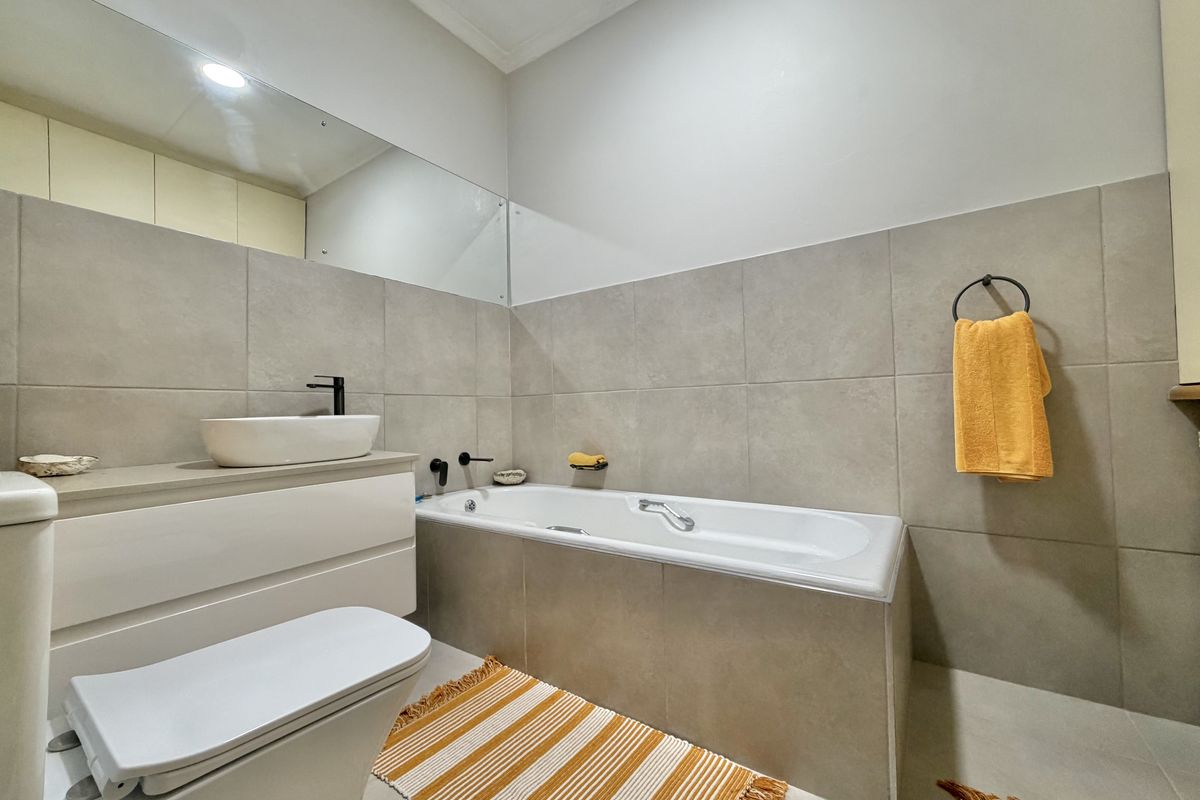 Modern bathroom featuring a built-in bathtub, wall-mounted vanity with a vessel sink, matte black fixtures, and large-format neutral wall tiles.