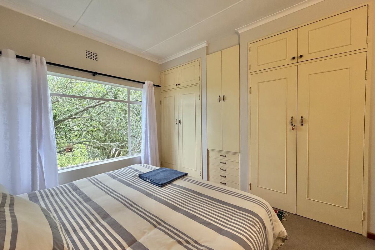 A bedroom featuring extensive built-in floor-to-ceiling cabinetry with integrated drawers and a large window providing natural light and garden views.