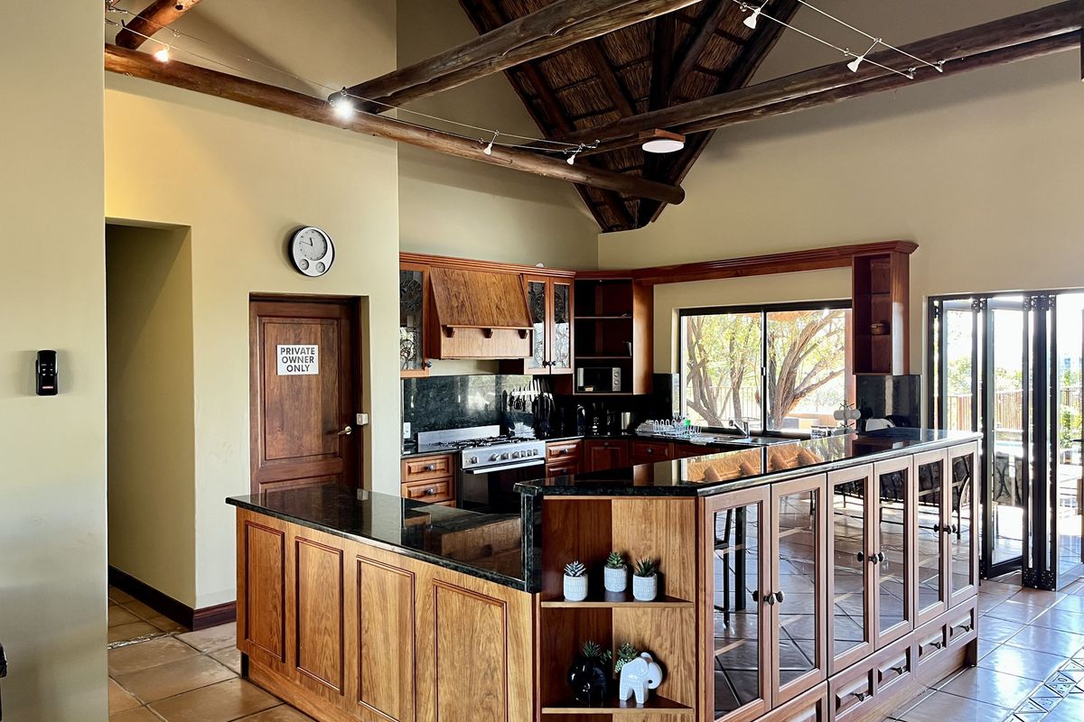 Spacious kitchen featuring wooden cabinetry, granite countertops, a built-in stove, and a high vaulted thatched ceiling with exposed timber beams.