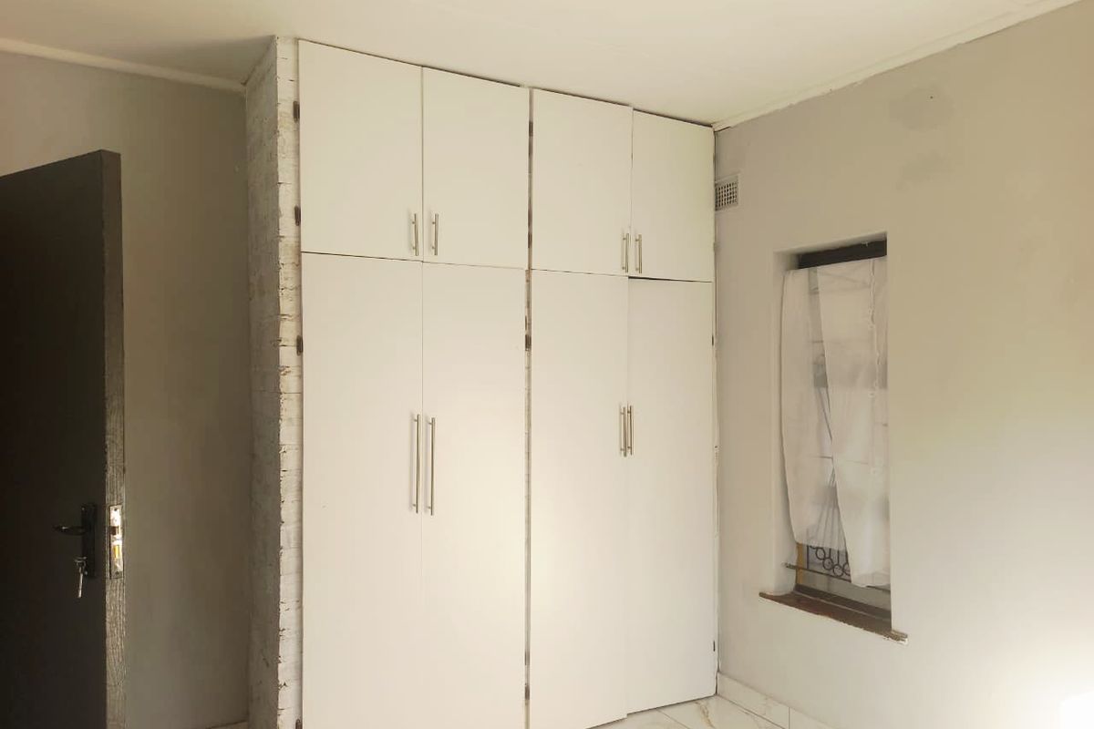 A bedroom featuring built-in white cabinetry with modern handles, tiled flooring, and a window with security bars.