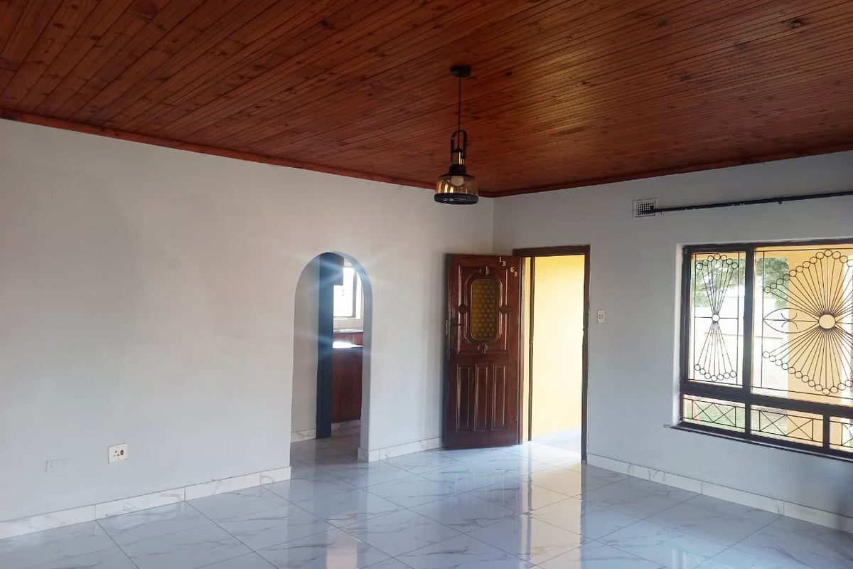 A bright living area featuring polished marble-look floor tiles, a timber-clad ceiling, and an arched entryway leading to the kitchen.