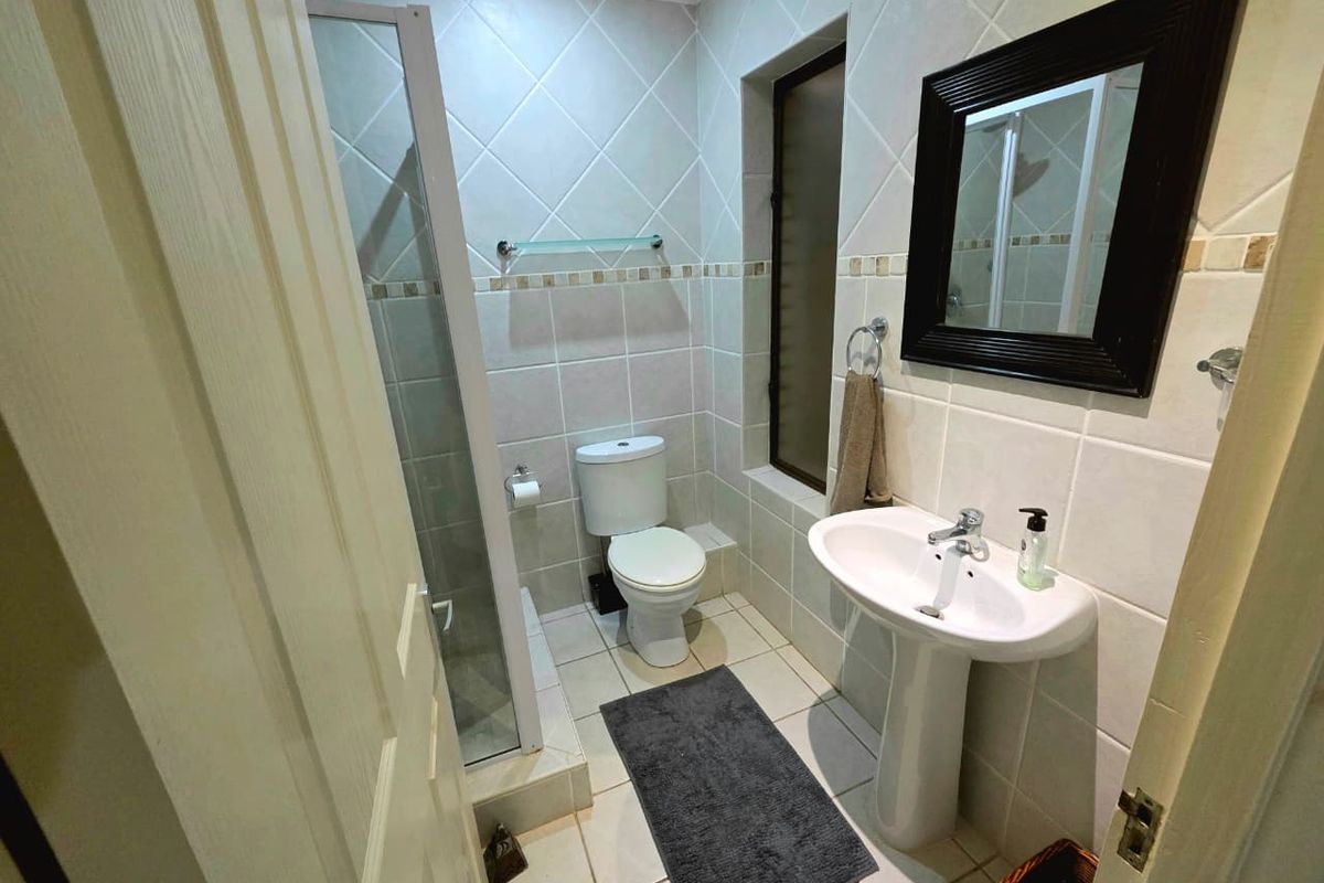 A compact bathroom featuring a pedestal sink, a toilet, and a glass-enclosed shower with neutral wall and floor tiling.