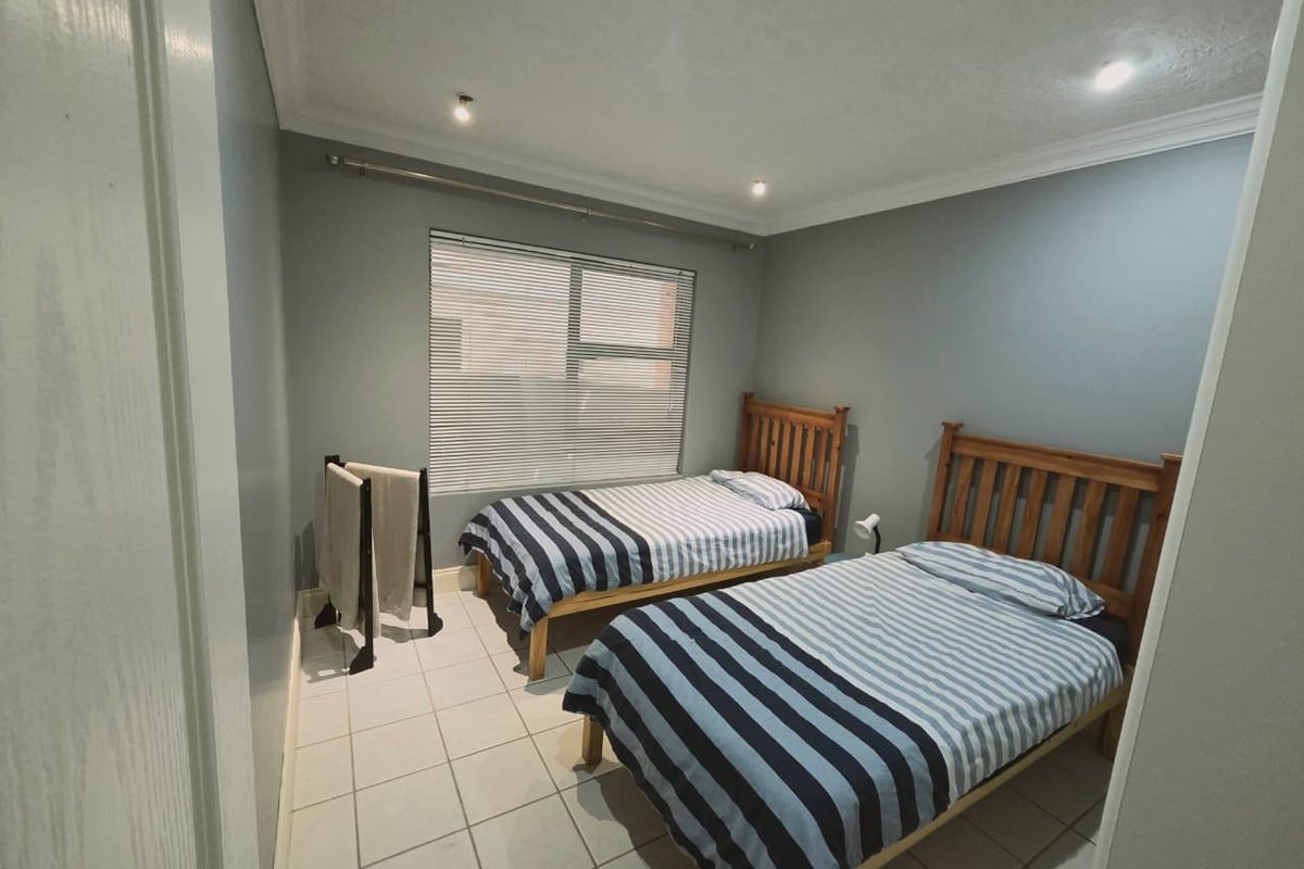 A functional bedroom featuring tiled flooring, neutral wall paint, and a window with fitted blinds.