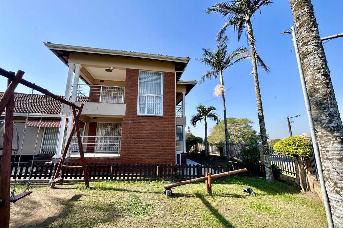 A view of the rear exterior of the house featuring a double-story brick facade, balconies with metal railings, and a landscaped garden area.