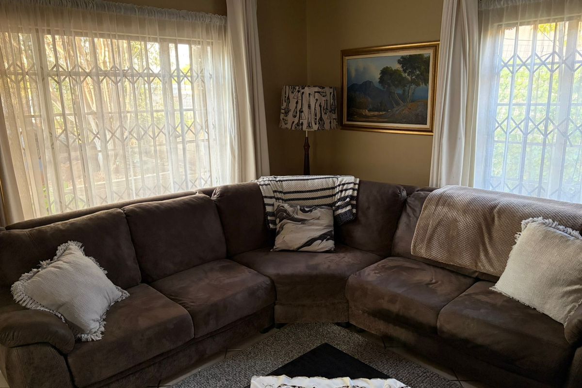 A cozy living room featuring large windows with security gates, neutral wall tones, and tiled flooring, providing a comfortable and functional living space.