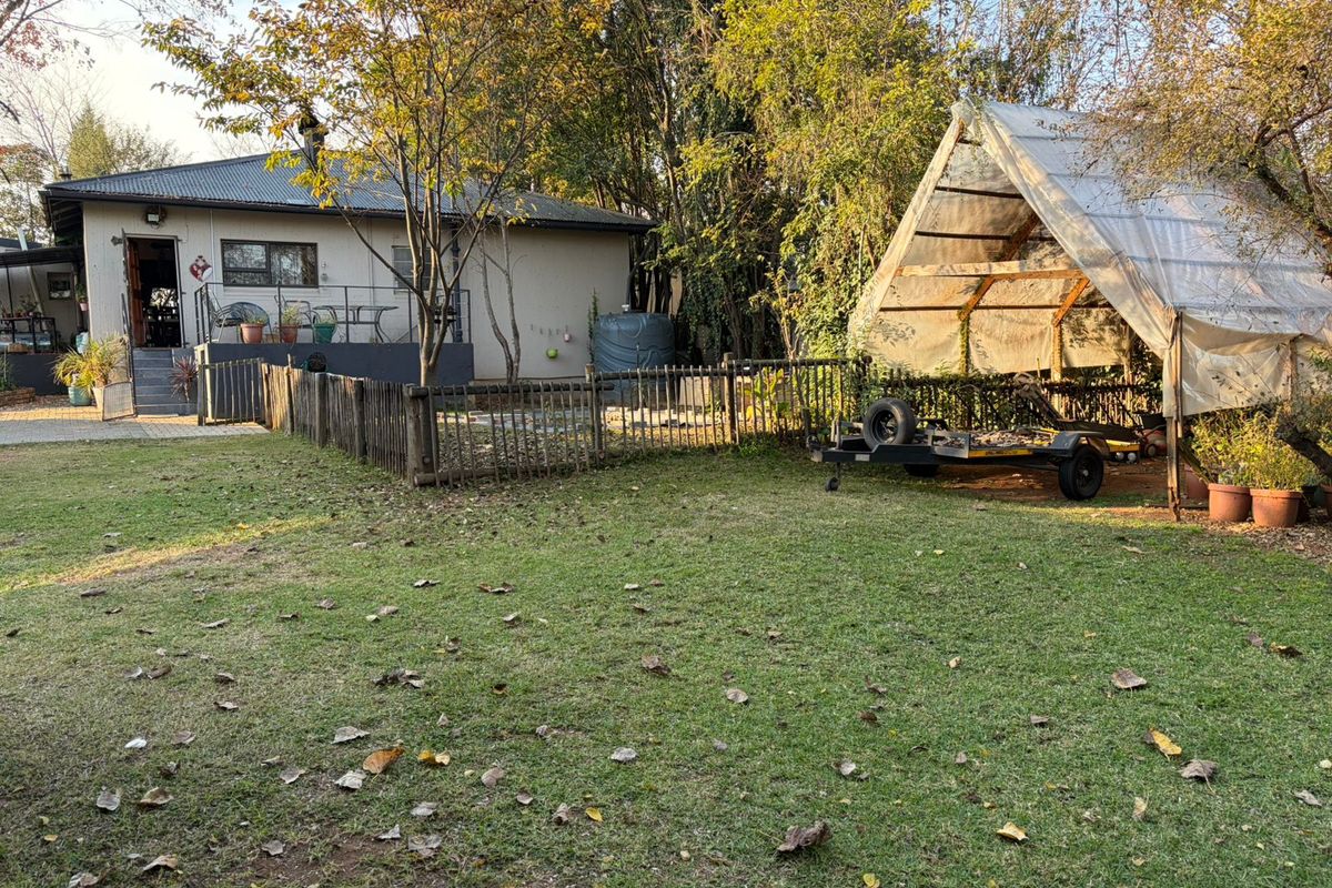 A spacious rear garden featuring a lawn area, established trees, a wooden fence, and a covered outdoor storage or utility structure.