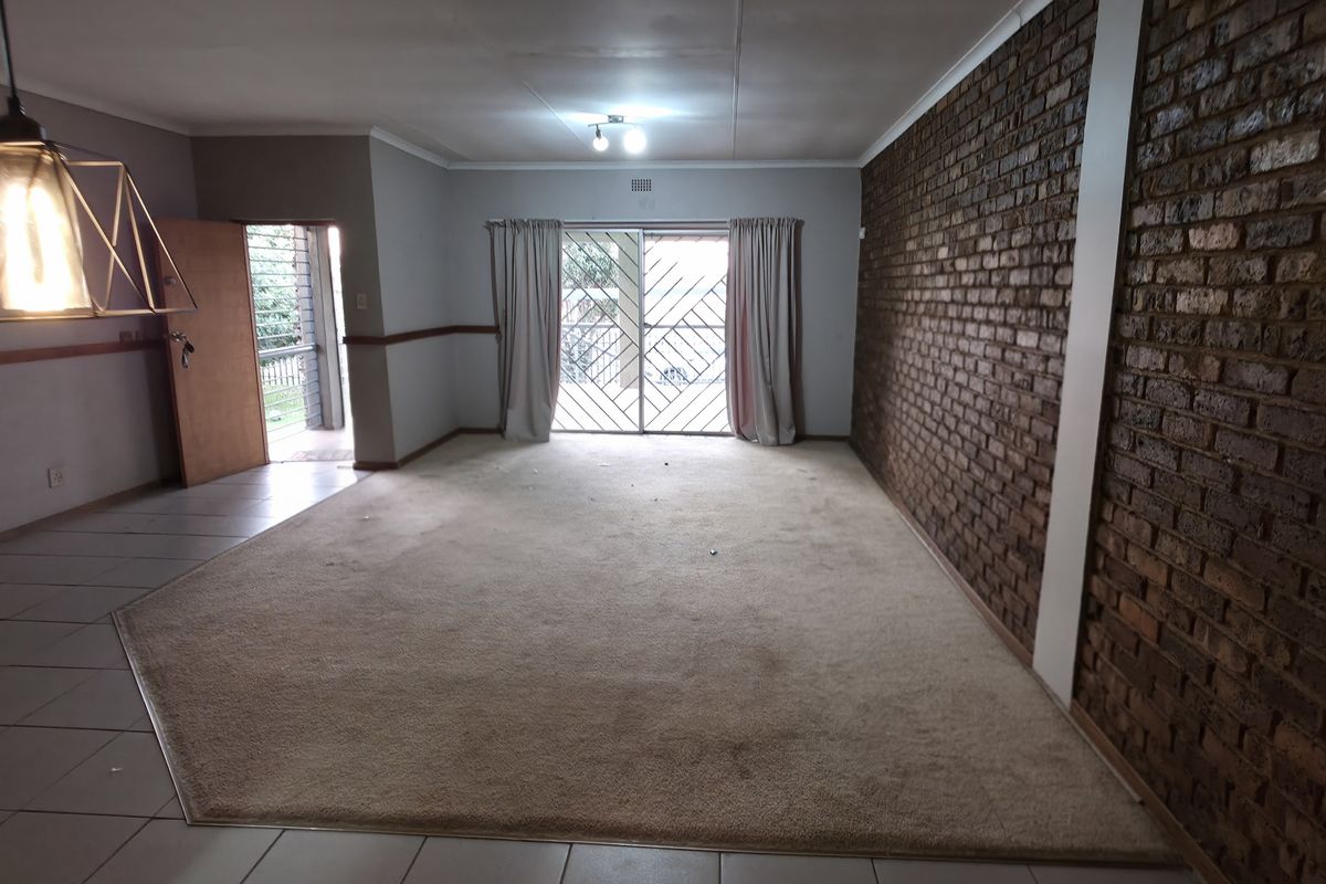 Spacious living area featuring an exposed brick feature wall, tiled and carpeted flooring, and direct access to the exterior through a sliding glass door.