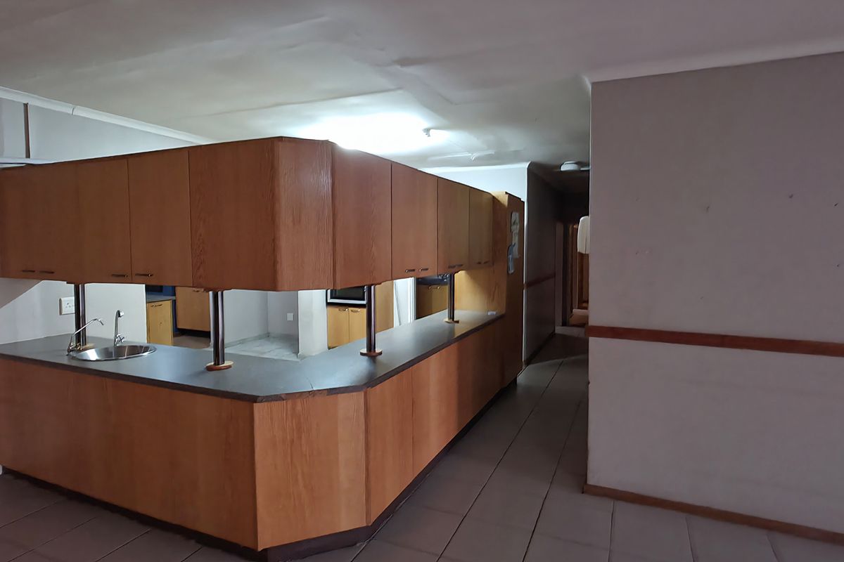 An empty kitchen featuring dated wood-finish cabinetry, a breakfast bar, and tiled flooring, showing signs of ceiling water damage and general wear.