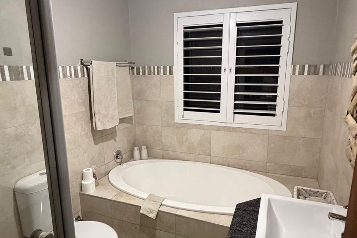 A well-maintained bathroom featuring a built-in oval bathtub, a modern vessel sink on a granite vanity, and white plantation shutters.