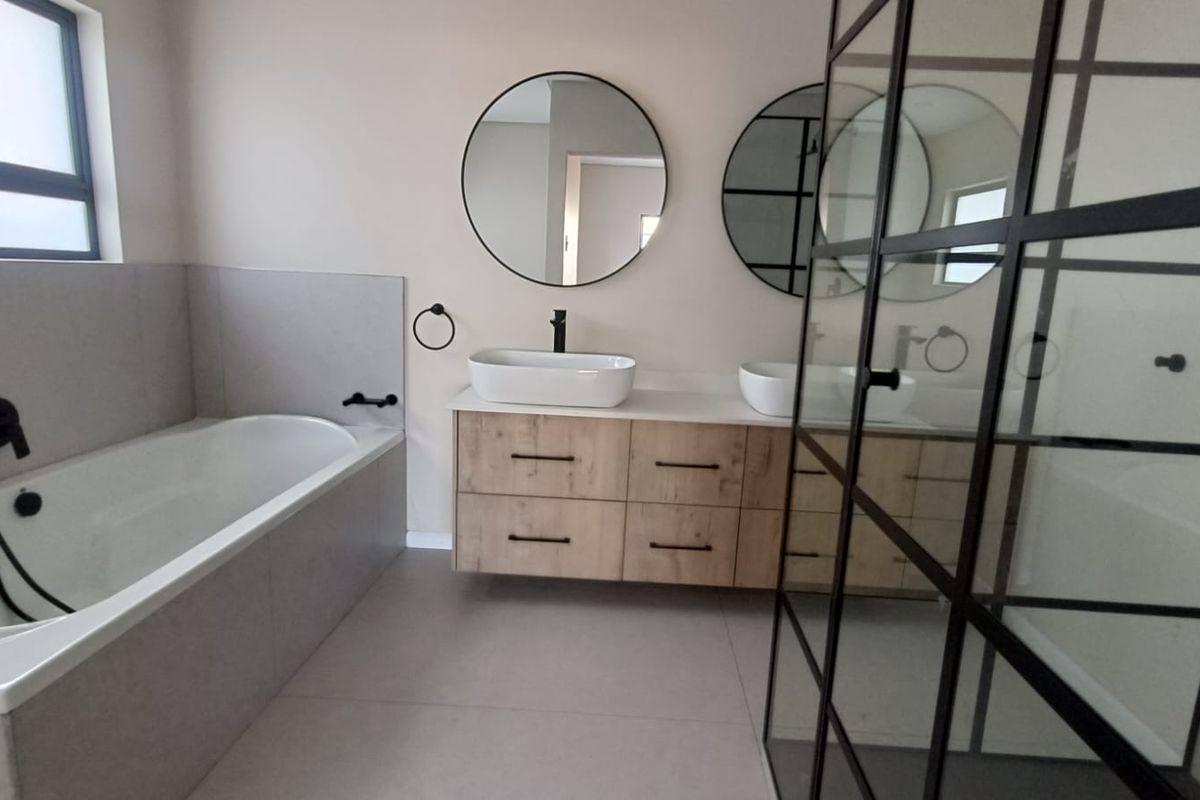 Modern bathroom featuring a floating wood-finish vanity with dual vessel sinks, a built-in bathtub, and a black-framed glass shower enclosure.