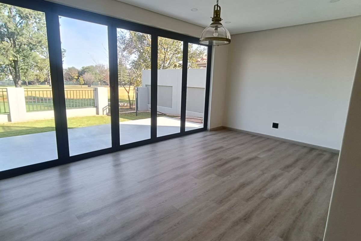 A bright, modern living area featuring wood-look flooring, recessed lighting, and large black-framed sliding glass doors opening onto a patio and garden.