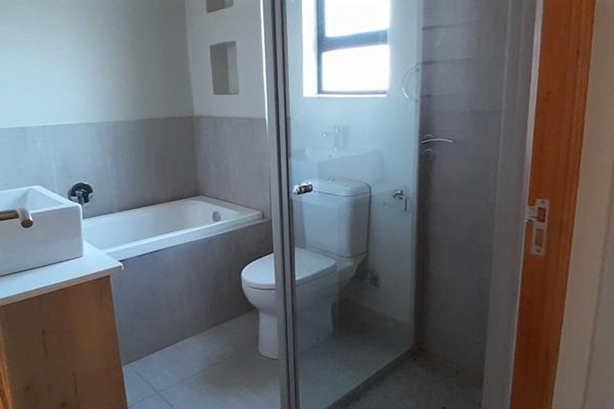 A modern bathroom featuring a built-in bathtub, a separate glass-enclosed shower, a toilet, and a vanity basin with neutral tiling.