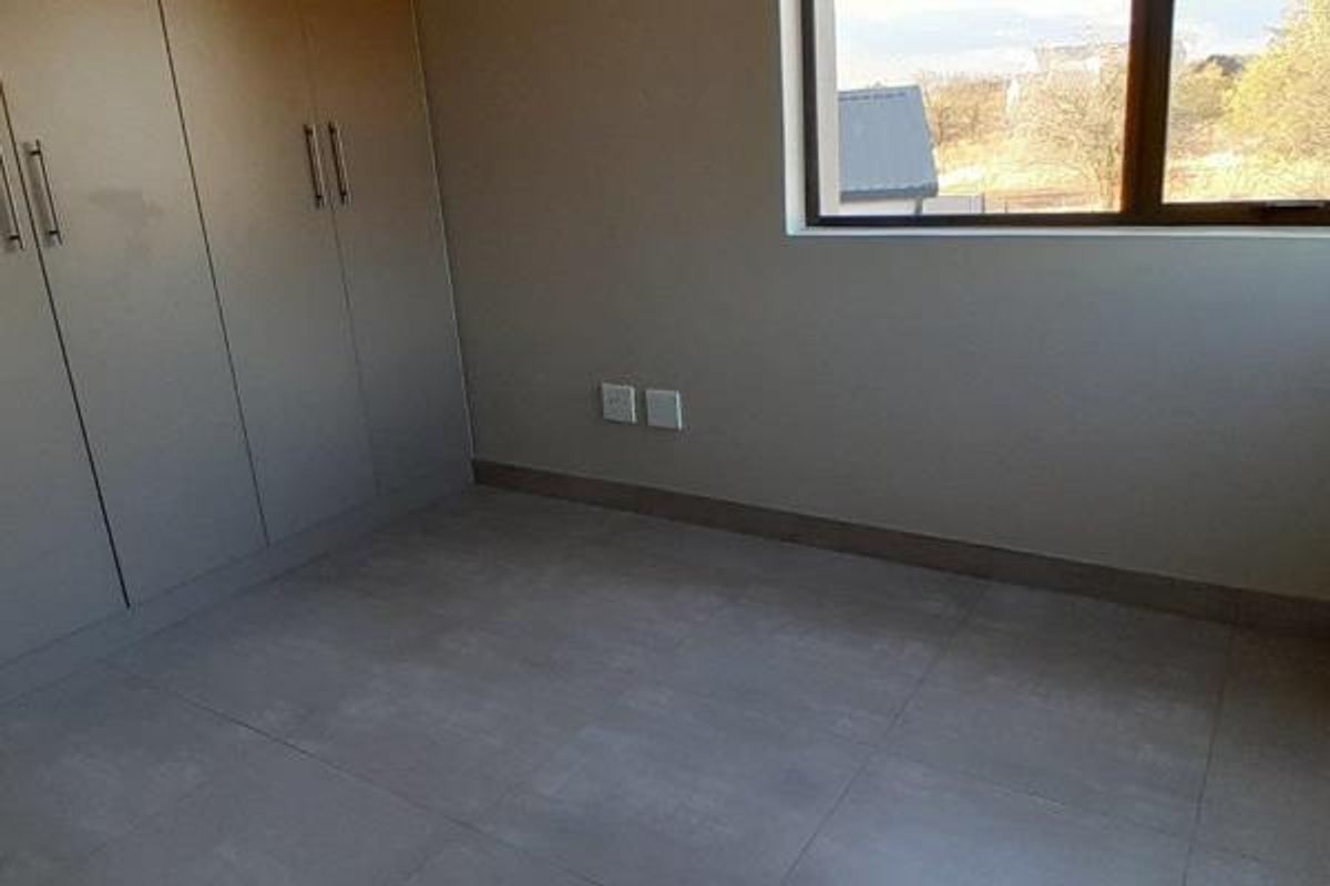 A clean, modern bedroom featuring neutral tiled flooring, built-in cabinetry, and a large window providing natural light and exterior views.