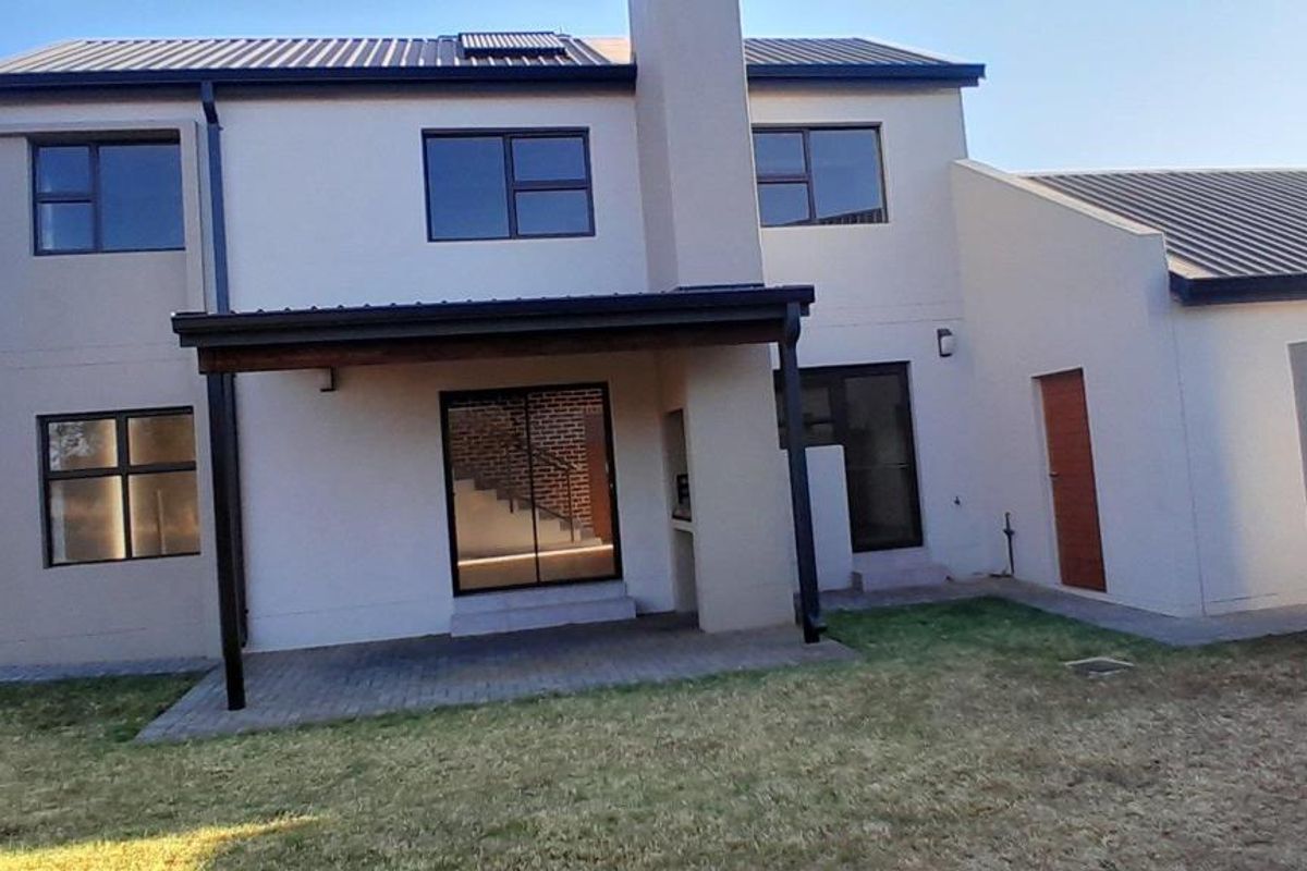 Rear view of a modern two-story house featuring a covered patio, built-in braai, and a spacious backyard.