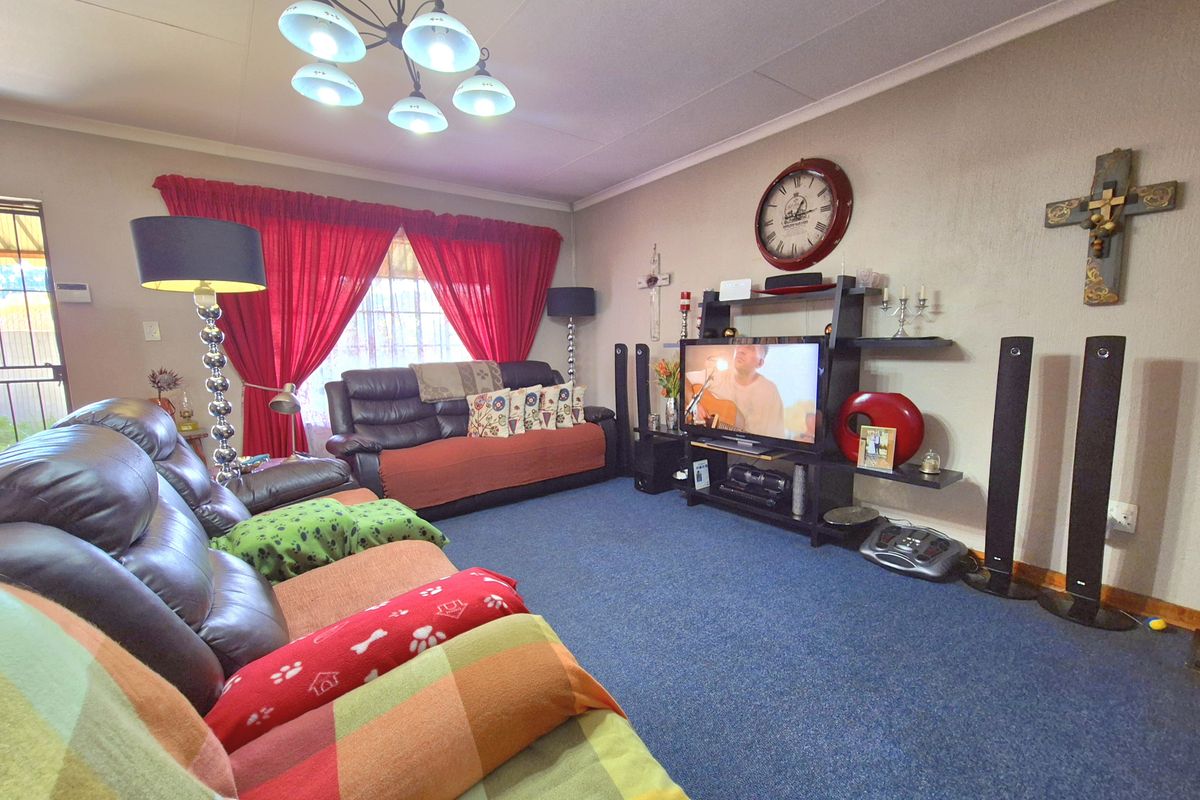 A spacious living room featuring blue carpeting, a central ceiling light fixture, and large windows with red curtains.