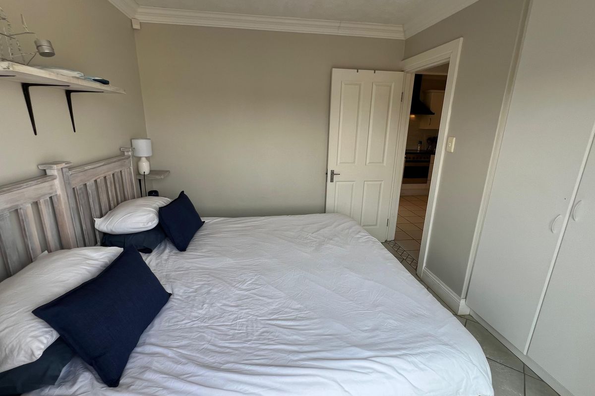 A bedroom featuring built-in cupboards, crown molding, and tiled flooring, with a doorway leading to an adjacent kitchen area.