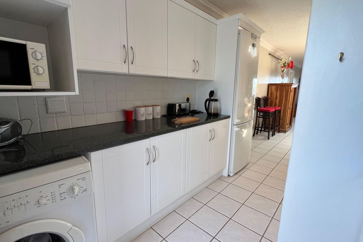 A functional kitchen featuring white cabinetry, dark granite countertops, tiled backsplash, and integrated laundry space, leading into an adjacent living area.