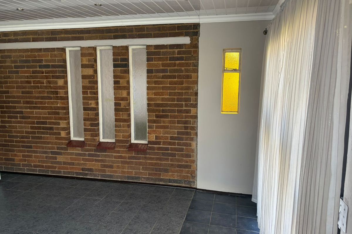 A living area featuring a textured brick feature wall, tiled flooring, and a unique yellow-tinted accent window.