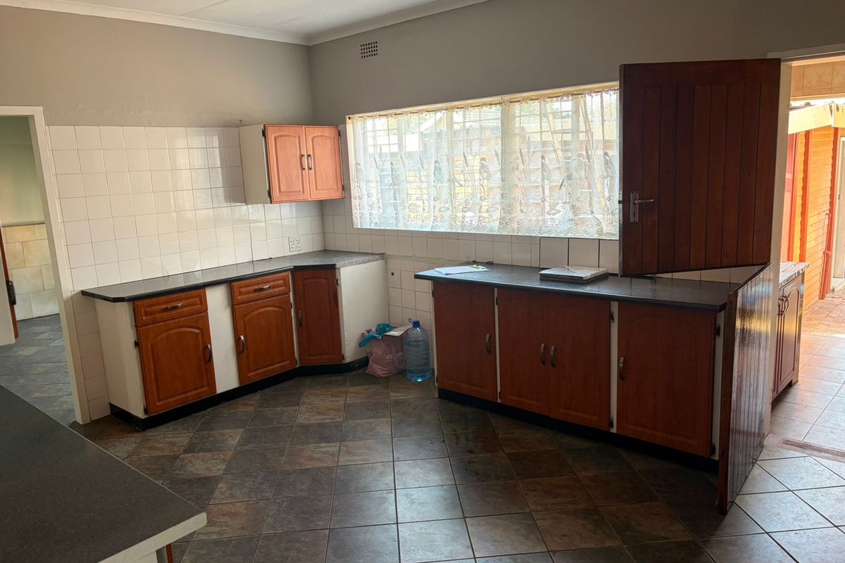 A functional kitchen featuring wooden cabinetry, dark laminate countertops, tiled splashbacks, and tiled flooring with a window overlooking the exterior.