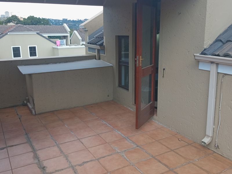 An open-air balcony featuring tiled flooring, a built-in counter, and direct access to the interior through a timber door.