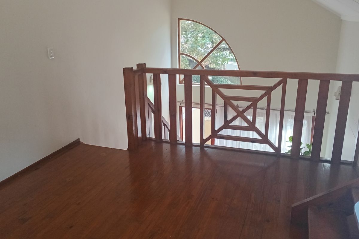 An open mezzanine landing area featuring polished wooden flooring, a traditional wooden balustrade, and a distinctive arched window overlooking the lower level.