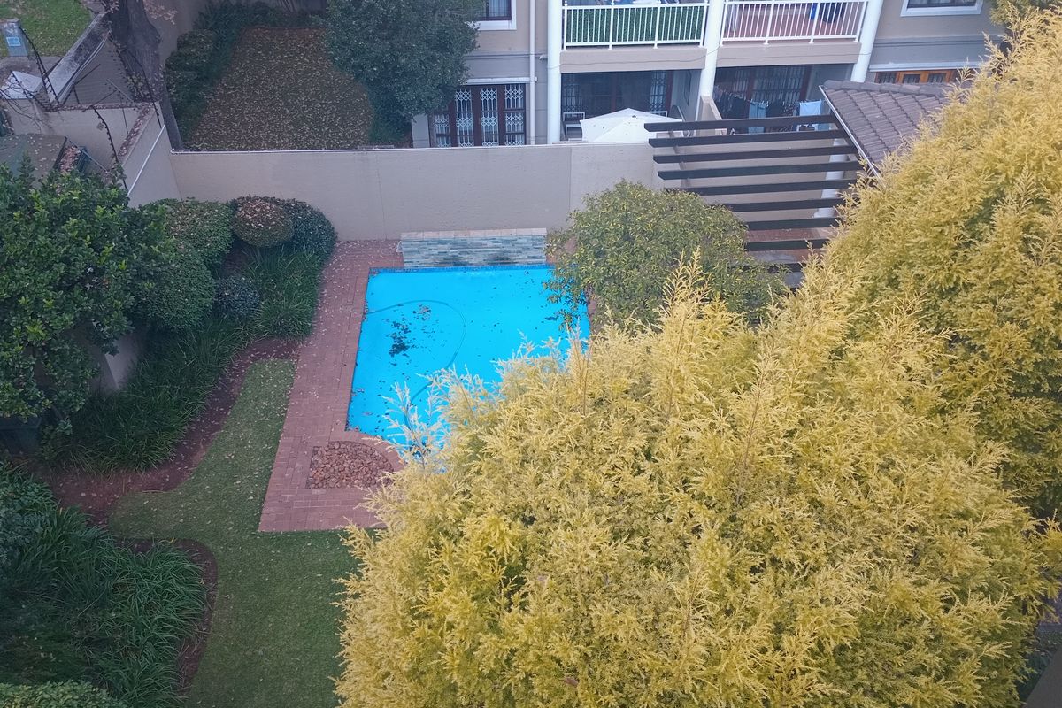 Aerial view of a townhouse backyard featuring a swimming pool, brick paved surround, landscaped garden, and a wooden pergola structure.