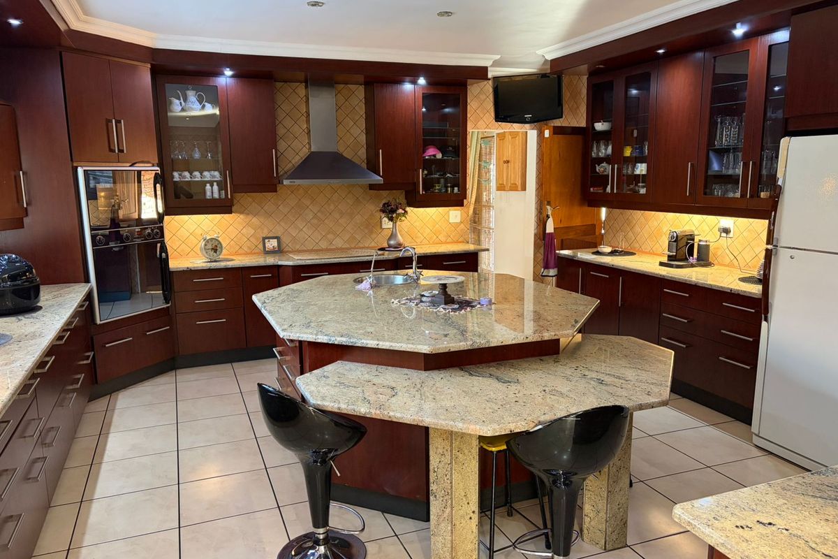 Spacious kitchen featuring dark wood cabinetry, granite countertops, a central island with integrated seating, and built-in appliances including an oven and extractor fan.