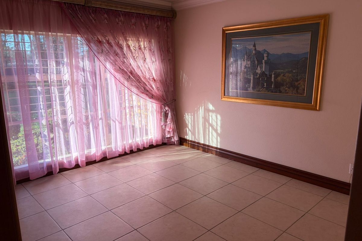 A bright, empty living room featuring large windows with security bars, tiled flooring, and crown molding, offering a clean and versatile space.