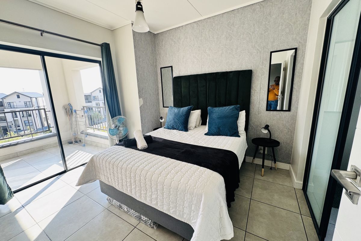 A well-lit bedroom featuring tiled flooring, a feature wall with wallpaper, and large sliding glass doors providing access to a private balcony.